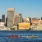 a group of people rowing boats in a body of water with a city in the background